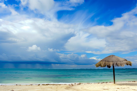 serene beach scene with a straw umbrella and a dramatic cloudy s