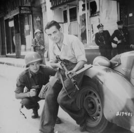 An American officer and a French partisan crouch behind an auto