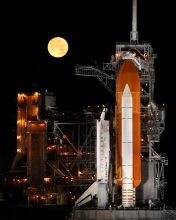 nearly full Moon sets as the space shuttle Discovery sits atop L