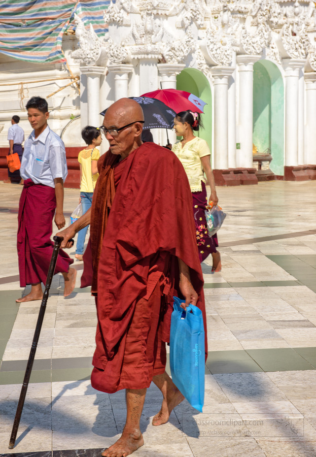 Buddhist monk in traditional robes walking Shwedagon Pagoda in Y