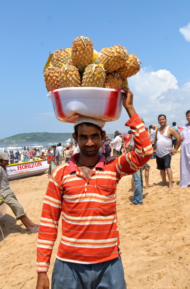 Man holding tub of pineapples on his head on beach