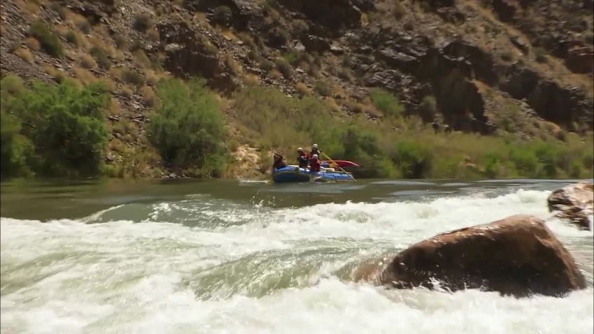 blue raft with two paddlers assisting enters the rapid