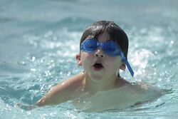 child swimming with blue goggles in a pool
