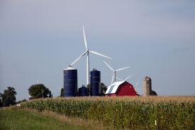 Farm scene including a bright-red barn three silos wind turbines