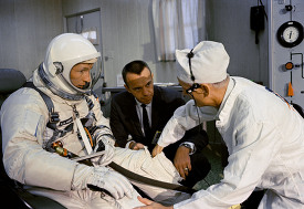 pilot gets help with the donning of his spacesuit from a suit te