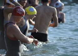 Triathletes prepare for a swimming race, adjusting their gear in
