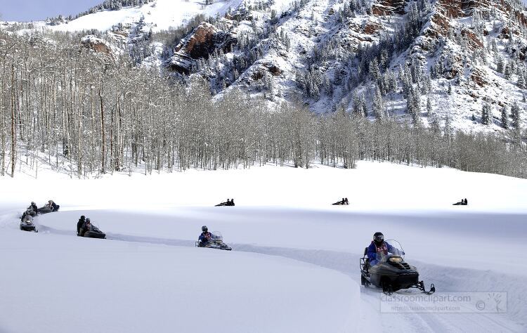 group of snowmobilers travels through a snowy mountain landscape