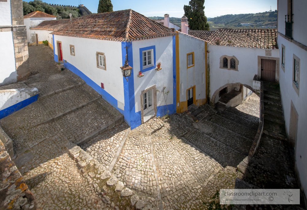 looking down at white washed building cobble stone street obidos
