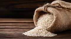 Burlap Sack Spilling Rice Grains on Wooden Table