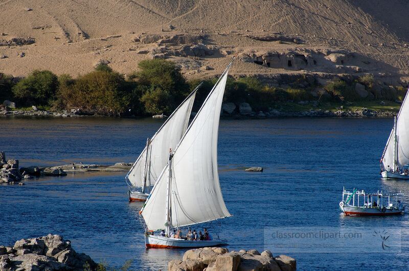 Feluccas with white sails glide gracefully across the Nile River surrounded by the stunning landscape of Aswan Egypt The hills and lush greenery create a picturesque backdrop