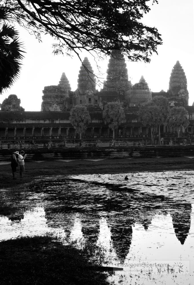 At dawn visitors explore the stunning Angkor Wat in Siem Reap Cambodia. The temples ancient architecture is reflected in the tranquil waters creating a serene atmosphere for contemplation.