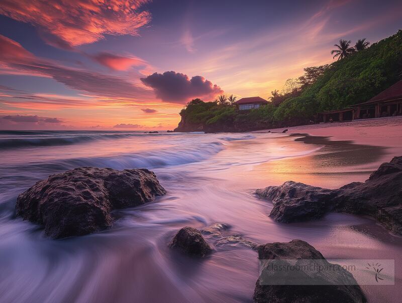 Waves gently wash over rugged rocks as a vibrant sunset paints the sky in stunning hues. Tranquil beach atmosphere invites moments of reflection and awe under the tropical trees.