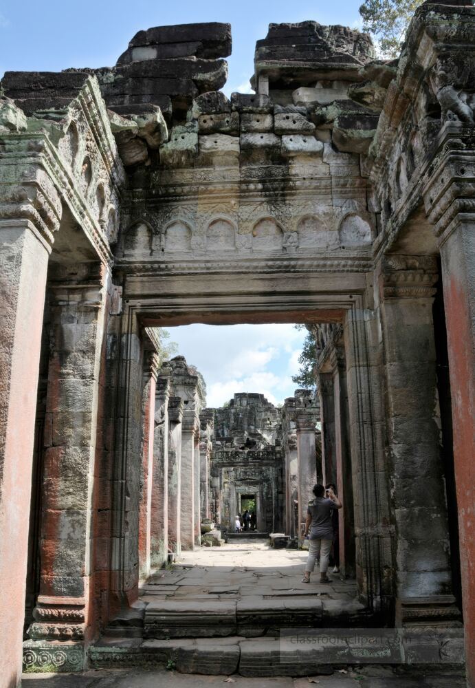 Visitors wander through the impressive stone corridors of Angkor Wat marveling at intricate carvings and ancient architecture under a bright blue sky embodying the spirit of Cambodias rich history.