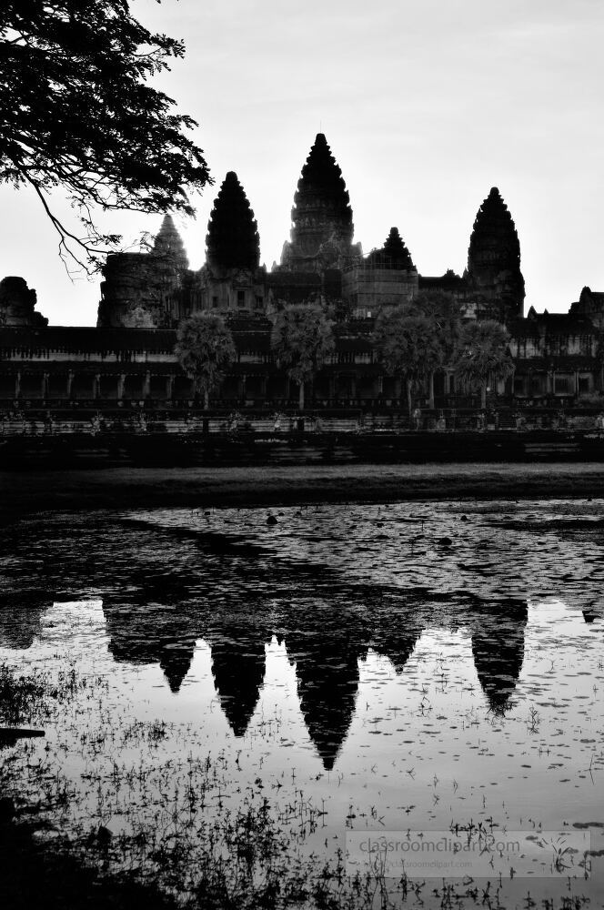 The majestic silhouette of Angkor Wat rises above serene waters just before dawn in Siem Reap. The intricate towers reflect beautifully in the stillness creating an enchanting atmosphere.