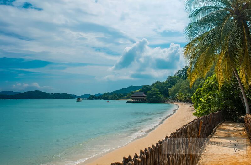 A serene beach in Langkawi featuring golden sand and clear turquoise waters Lush greenery lines the shoreline under a partly cloudy sky creating a tranquil atmosphere for visitors