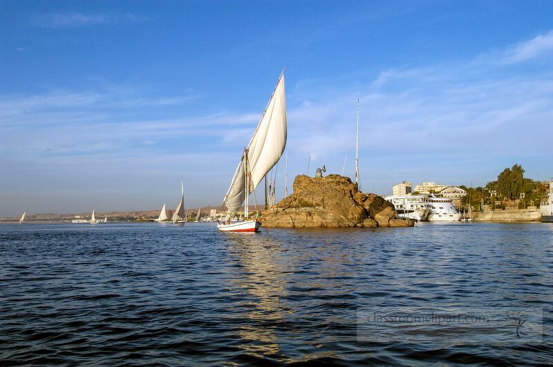 Bright sails catch the wind as traditional boats glide along the Nile River near Aswan surrounded by tranquil waters and scenic landscapes under a clear blue sky