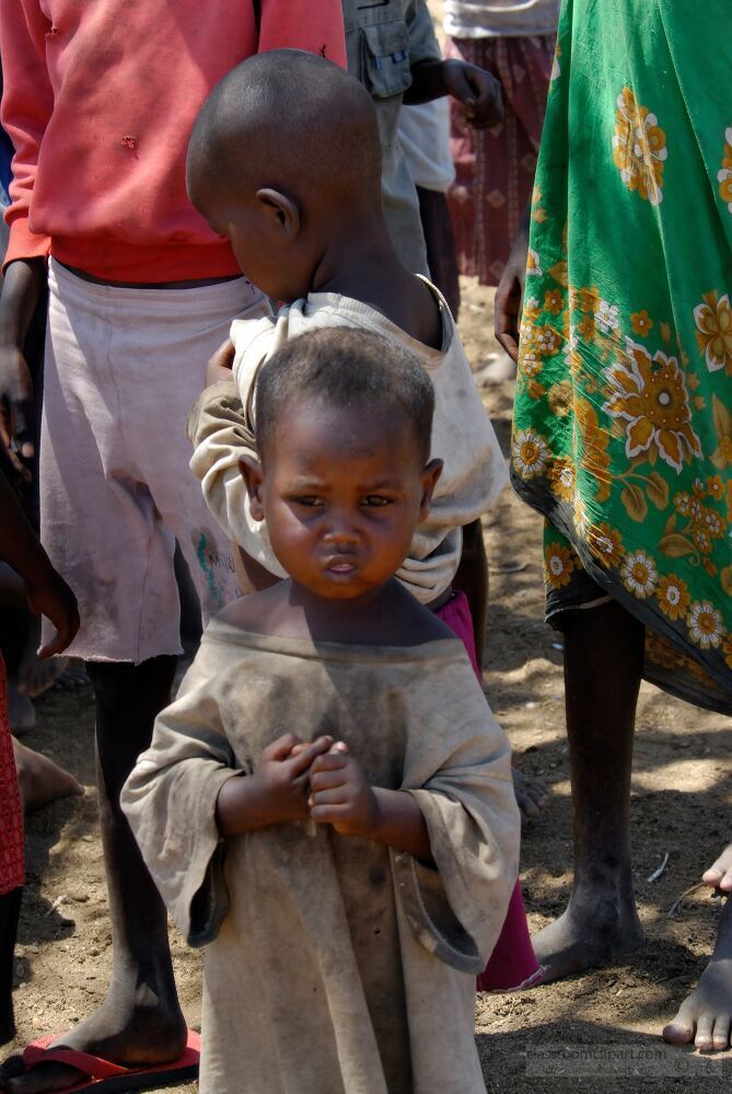 Young Samburu children stand together in their village surrounded by adults in traditional clothing The atmosphere reflects communal life with children playing and engaging The setting showcases their unique culture and daily activities