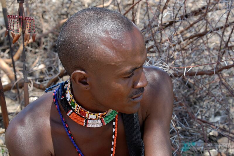 A Samburu warrior is seen resting amidst the arid landscape of Kenya Traditional adornments highlight his cultural heritage showcasing the vibrant identity of the Samburu tribe