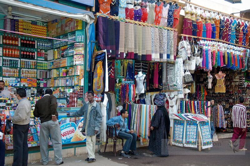 In Aswan Egypt vibrant souk stalls showcase various goods Local traders engage with customers while colorful textiles and products line the shopfronts The atmosphere is lively and inviting