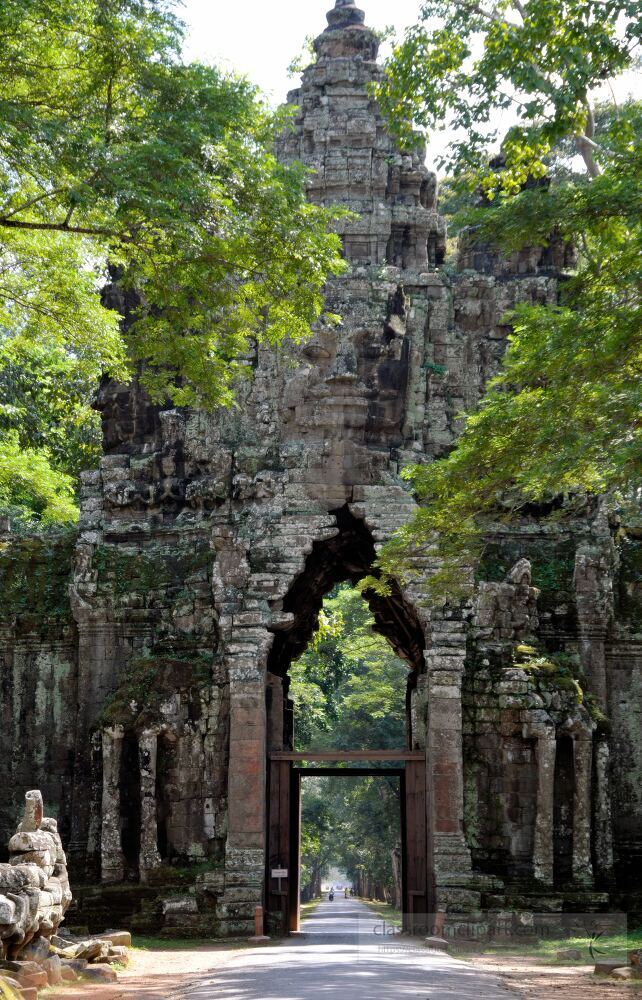 Majestic stone gate surrounded by lush greenery invites travelers to explore the ancient wonders of Angkor Wat in Siem Reap. Sunlight filters through towering trees creating a serene atmosphere.