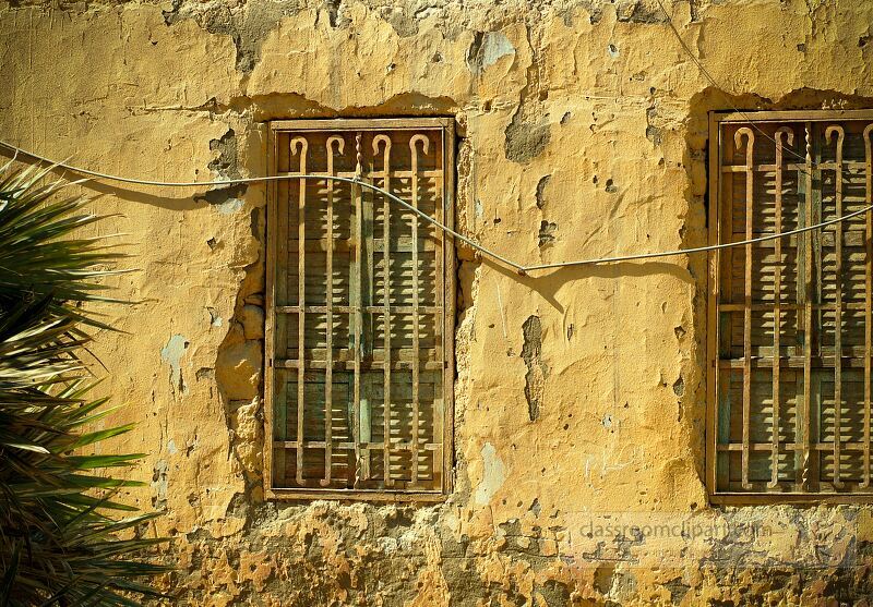 Two aged windows with metal bars are set into a weathered yellow wall in Aswan Egypt The rustic texture and colors hint at the areas rich history and culture