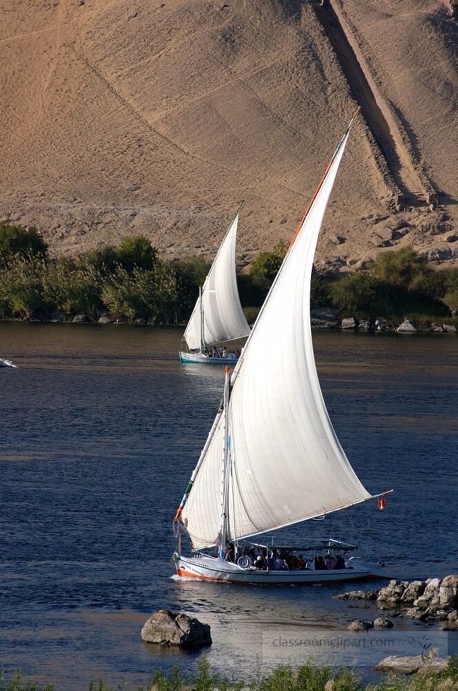 Two traditional feluccas sail gracefully on the Nile River near Aswan Egypt The serene landscape showcases sandy hills in the background and lush greenery along the shores