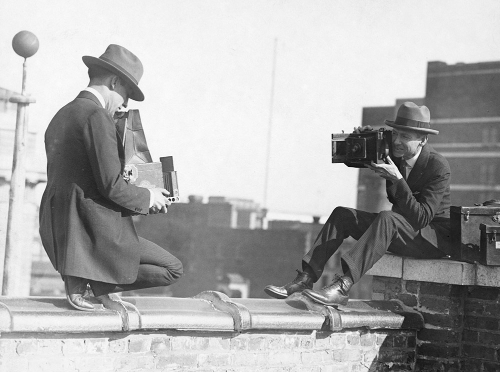 two-photographers-taking-each-other's-picture-with-hand-held-cameras-while-perched-on-a-roof.jpg